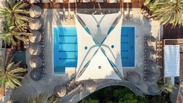 Vista aerea di una zona piscina con due piscine separate, circondata da lettini prendisole e palme.