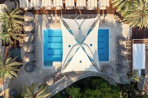 Vista aérea de una zona de piscina con dos piscinas separadas, rodeada de sillones de descanso y palmeras.