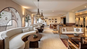 Un moderno vestíbulo de hotel con un sofá curvo, mesas de centro de madera y diversas opciones de asiento.