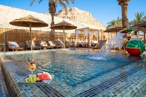 A pool area with lounge chairs, umbrellas, and a water feature. - Oasis Spa Club Dead Sea Hotel (Tamar)