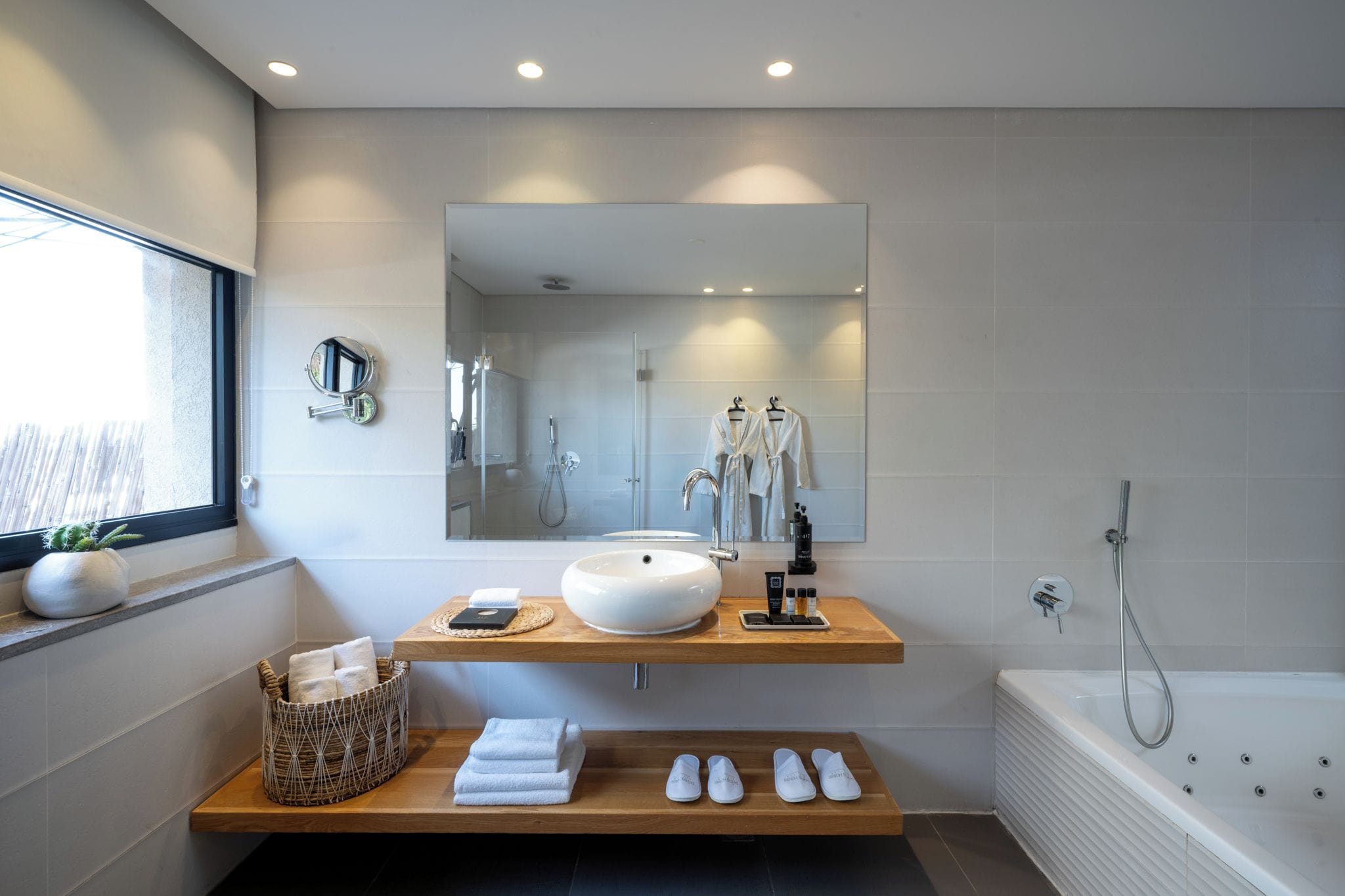 Une salle de bain moderne avec un grand miroir, un lavabo sur colonne, une baignoire et une fenêtre offrant une belle vue.