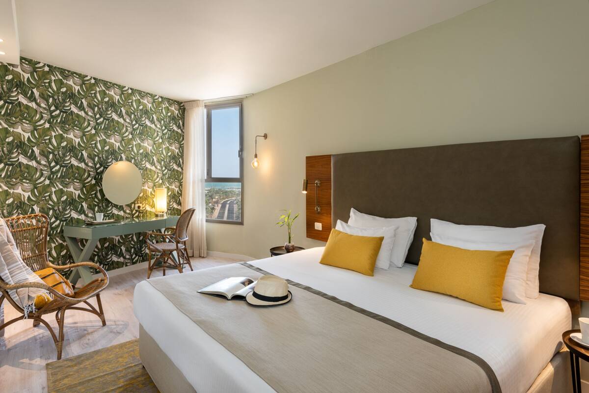 Hotellihuone, jossa on suuri sänky, työpöytä tuolilla, ikkuna ja näkymä kaupunkiin.