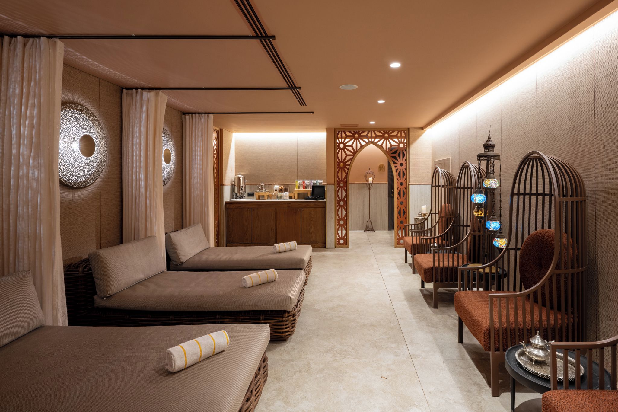 Ein Spa-Behandlungsraum mit zwei Massageliegen, einem kleinen Empfangstresen und einer Wand mit geometrischem Muster.