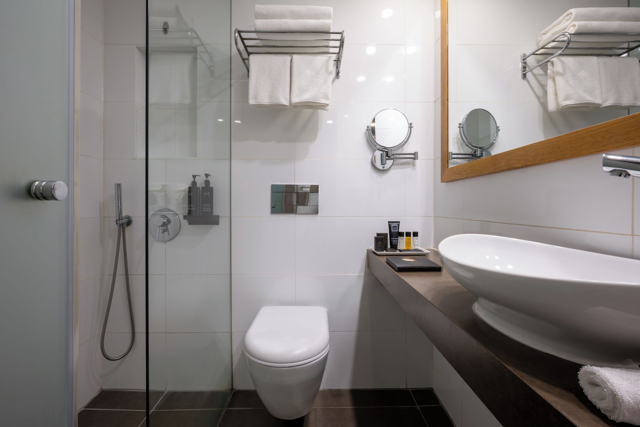 A modern bathroom with a glass shower enclosure, a white toilet, a vanity with a large sink, and a mirror.