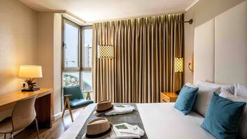 A hotel room with a bed, a desk, a chair, a lamp, and a window with curtains.