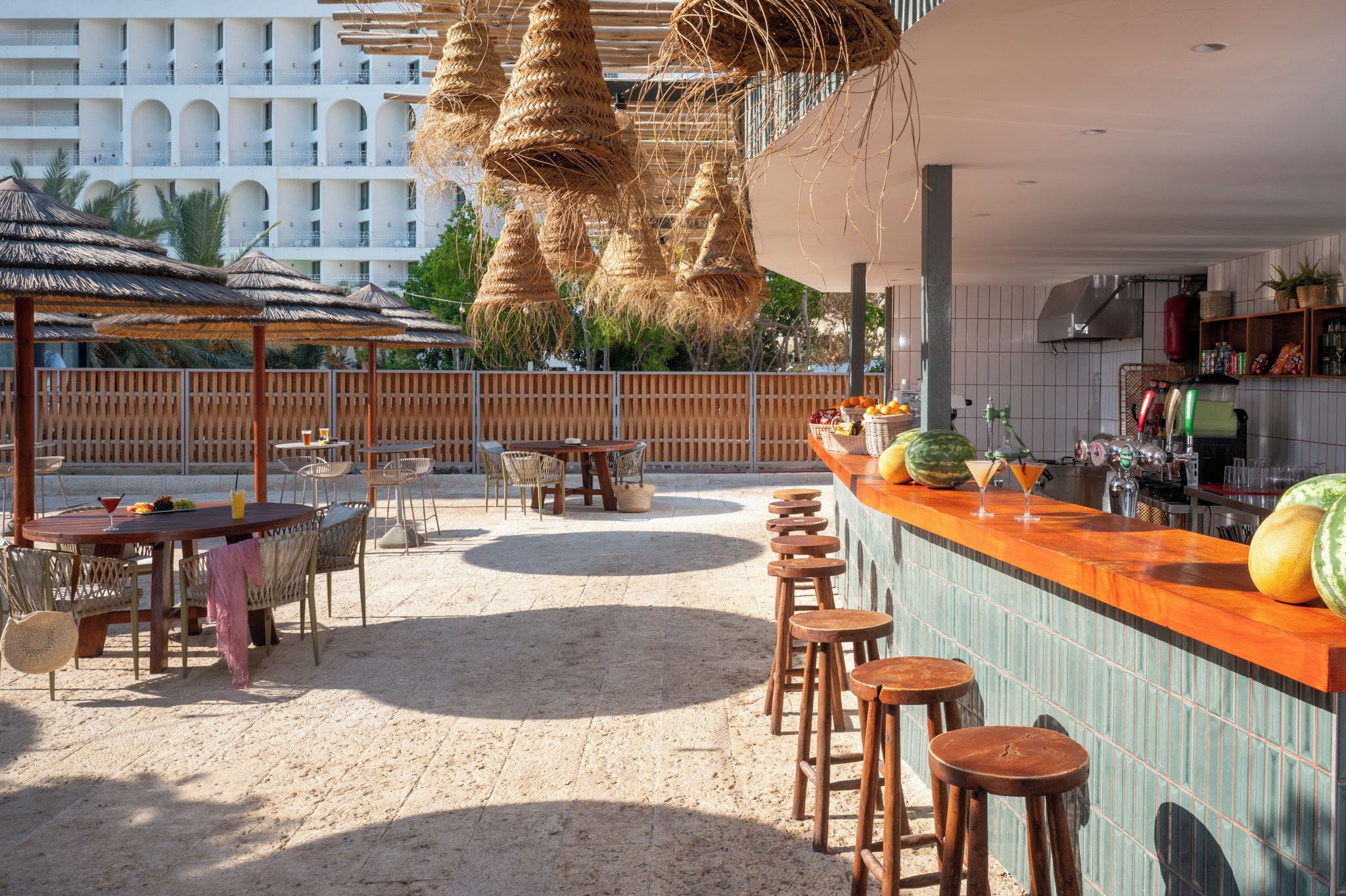 Un área de bar al aire libre con diversas opciones de asiento, una barra y vistas a un edificio al fondo.