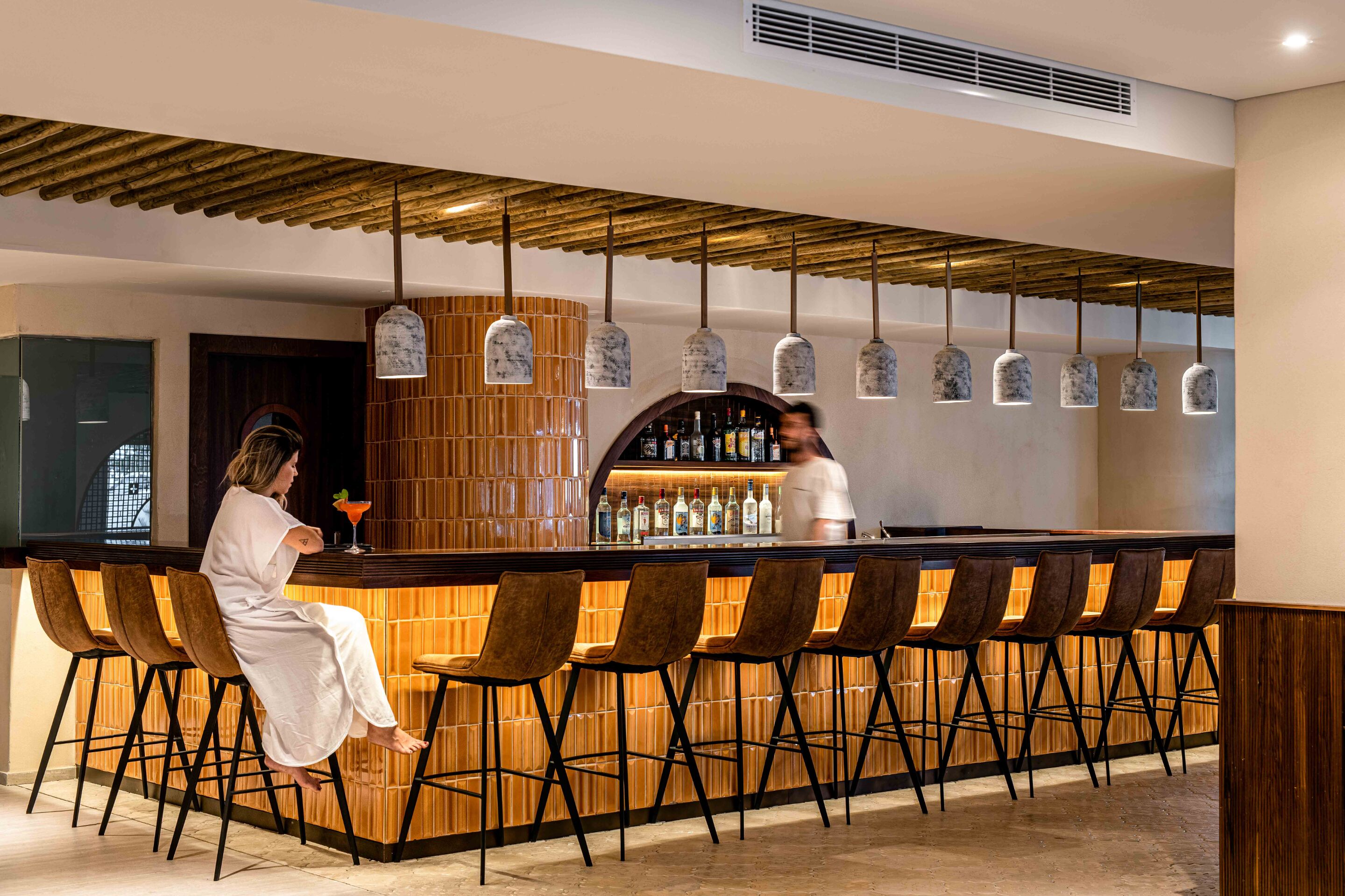 Eine Bar mit Holzbarhocker, einem Barkeeper und hängenden Pendelleuchten.