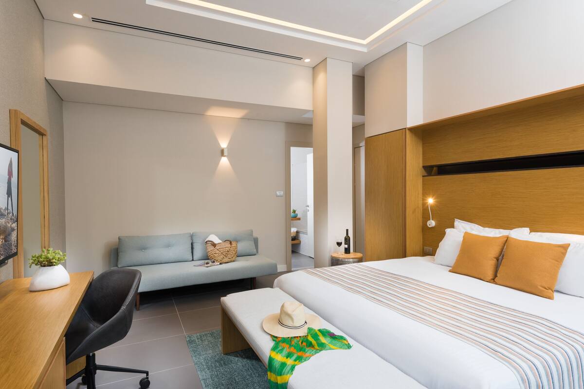 Moderni hotellihuone, jossa on suuri sänky, työpöytä, sohva ja pieni pöytä.
