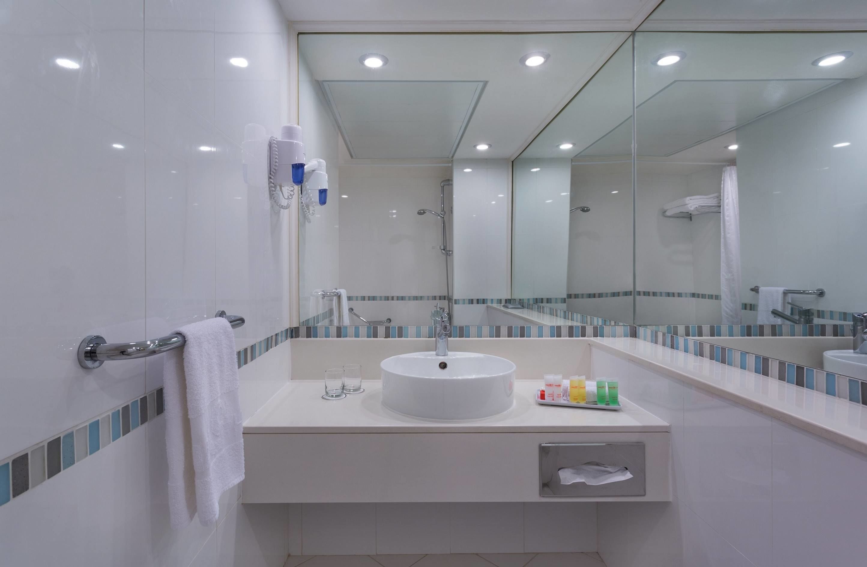 A modern bathroom with a large mirror, a round sink, and a glass shower enclosure.