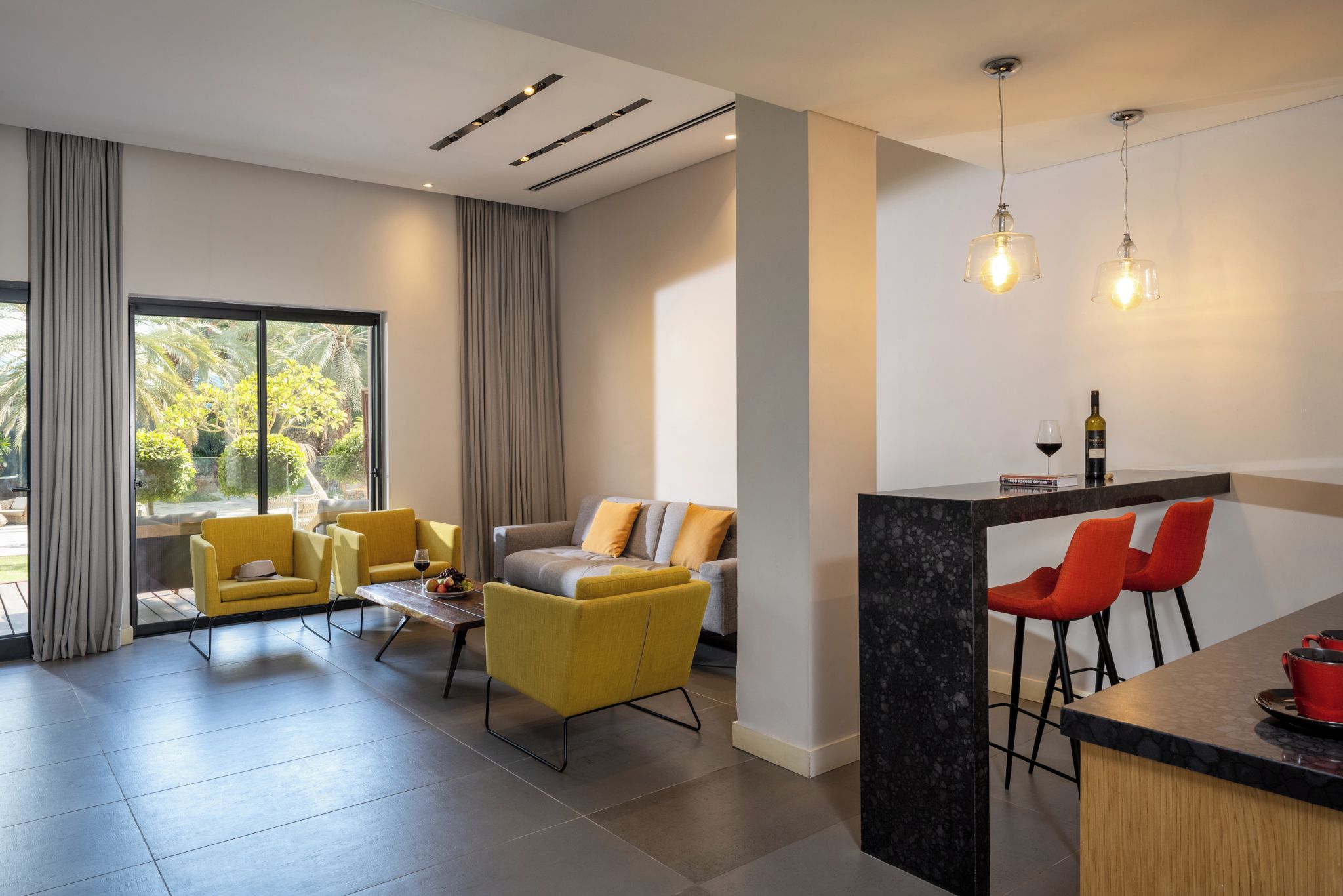 Una sala de estar moderna con un sofá, sillones, una zona de comedor con barra y ventanas grandes.