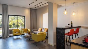 Una sala de estar moderna con un sofá, sillones, una zona de comedor con barra y ventanas grandes.