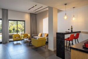 Una sala de estar moderna con un sofá, sillones, una zona de comedor con barra y ventanas grandes.