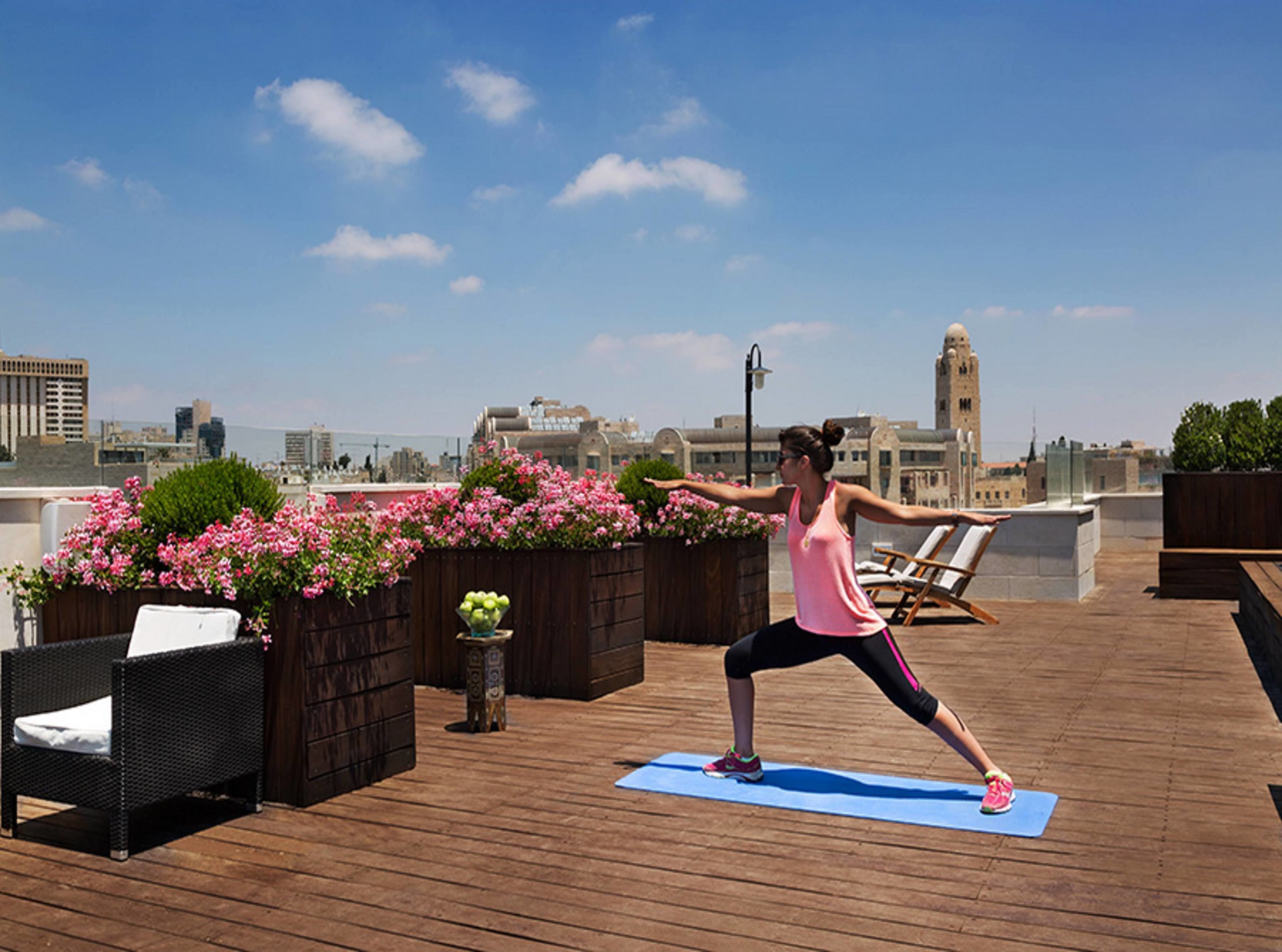 Una persona realiza una postura de yoga sobre una terraza de madera con un paisaje urbano al fondo.