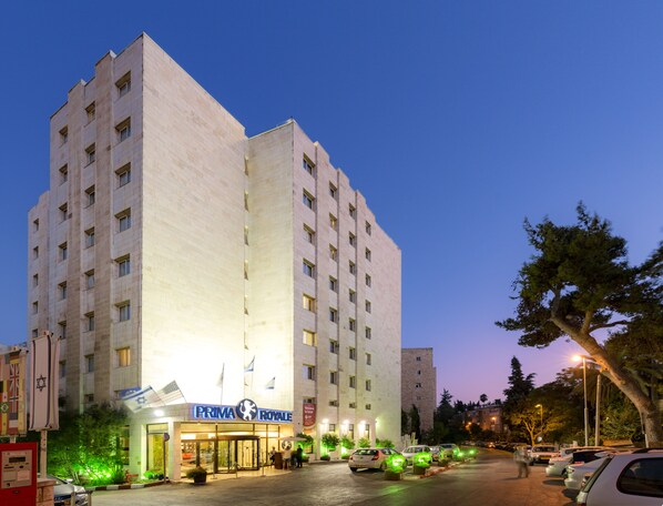 A multi-story hotel with a prominent entrance, a parking area, and a flag display. - Prima Royale (Jerusalem)