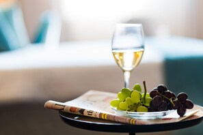 A glass of white wine, a bowl of green and dark grapes, and a magazine on a small table.