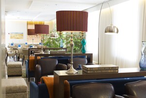 A modern hotel lobby with seating areas, a reception desk, and decorative plants.