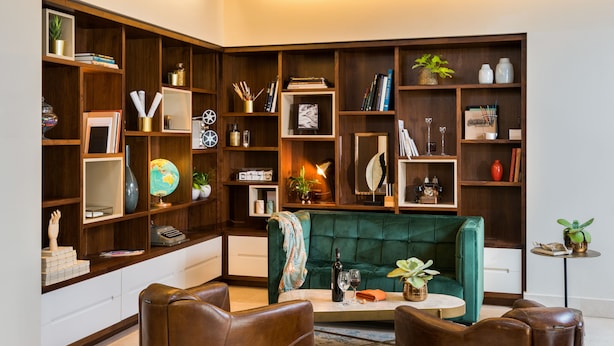 A cozy living room with a green sofa, leather armchairs, and a coffee table. It features wooden bookshelves filled with books, decorative items, and plants. - Prima Royale (Jerusalem)
