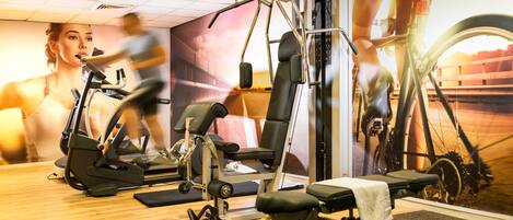 Un gimnasio con equipamiento de ejercicio, un mural en la pared y suelo de madera.