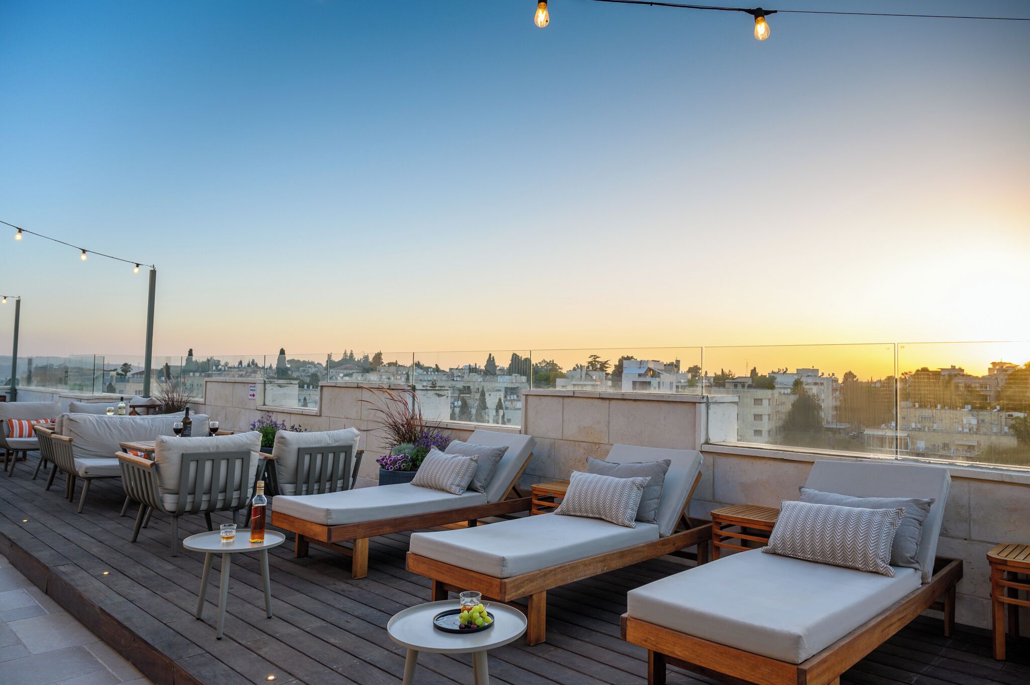 Una terraza en la azotea con sillones, mesas y luces colgantes.