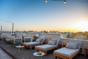 Una terraza en la azotea con sillones, mesas y luces colgantes.