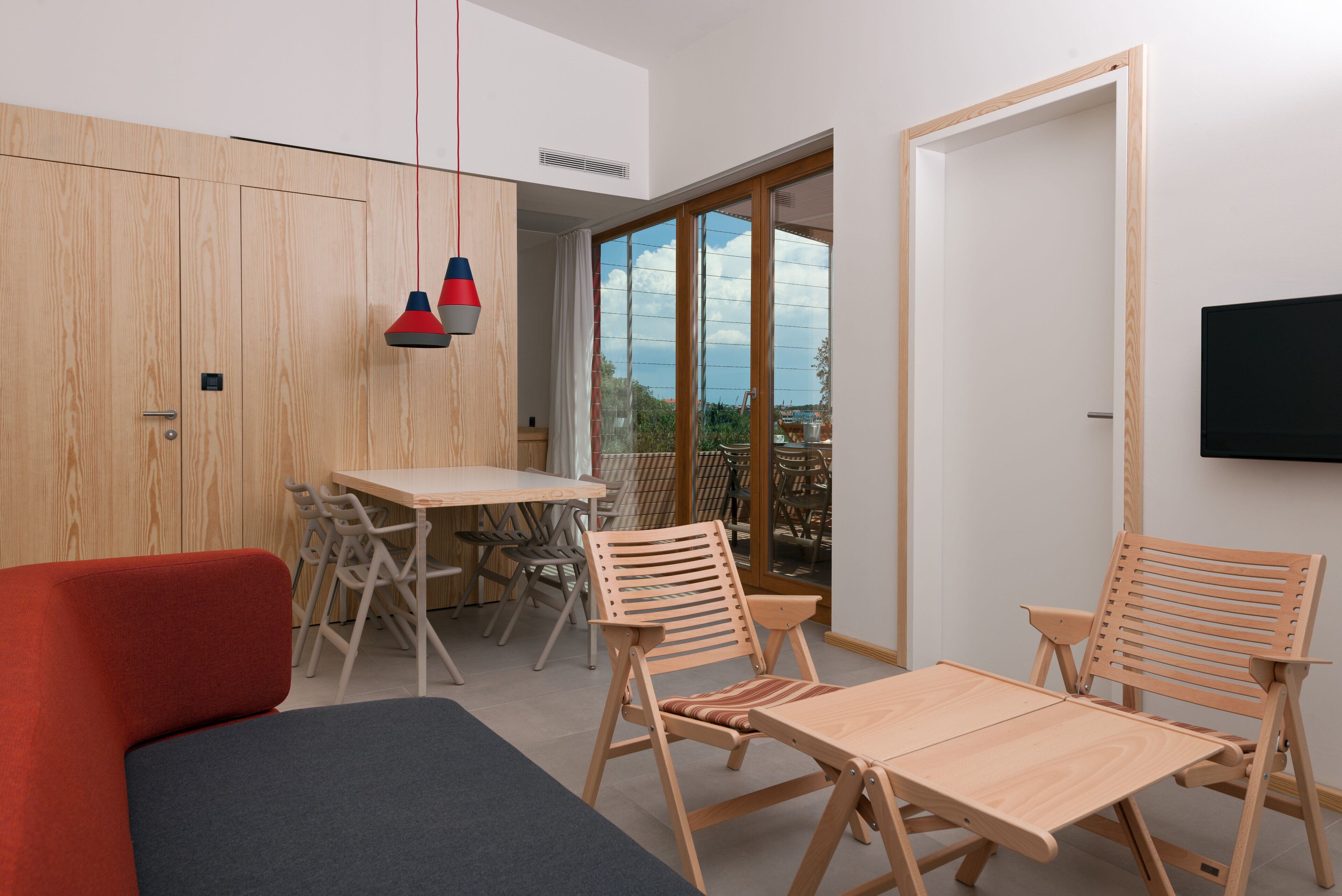 Ein modernes Zimmer mit einem Holztisch, zwei Holzstühlen, einem roten Sofa und einem Fernseher an der Wand.