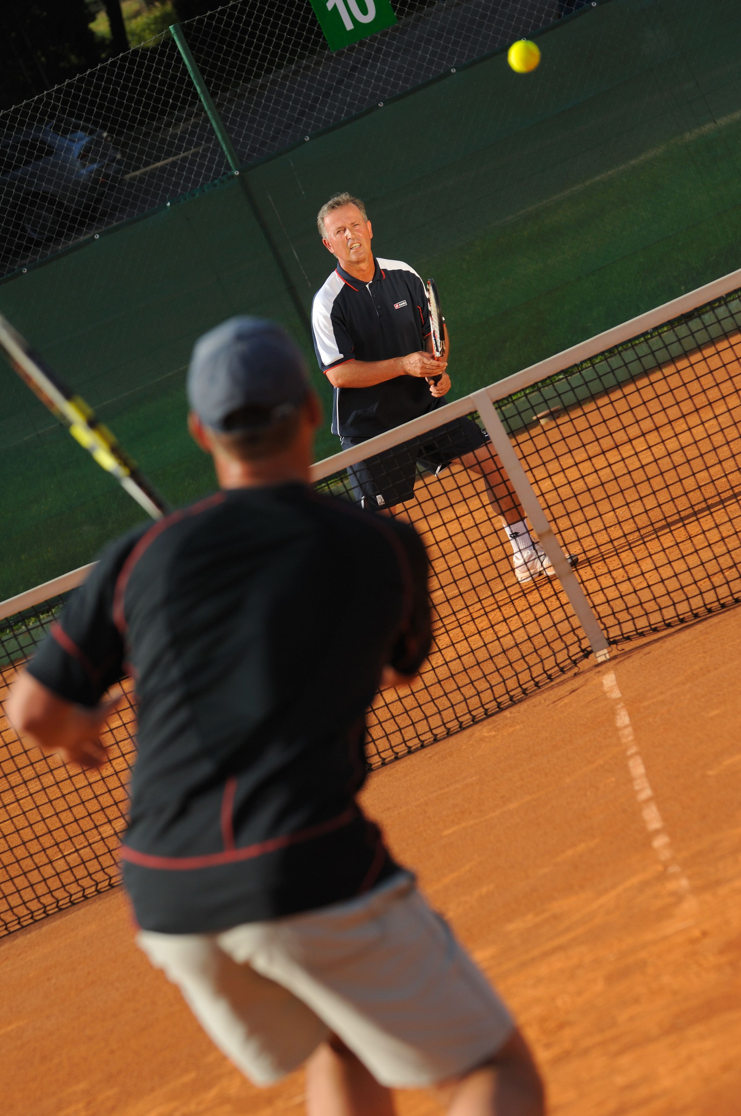 A tennis court with a net in the middle, a player in the foreground, and another player in the background.