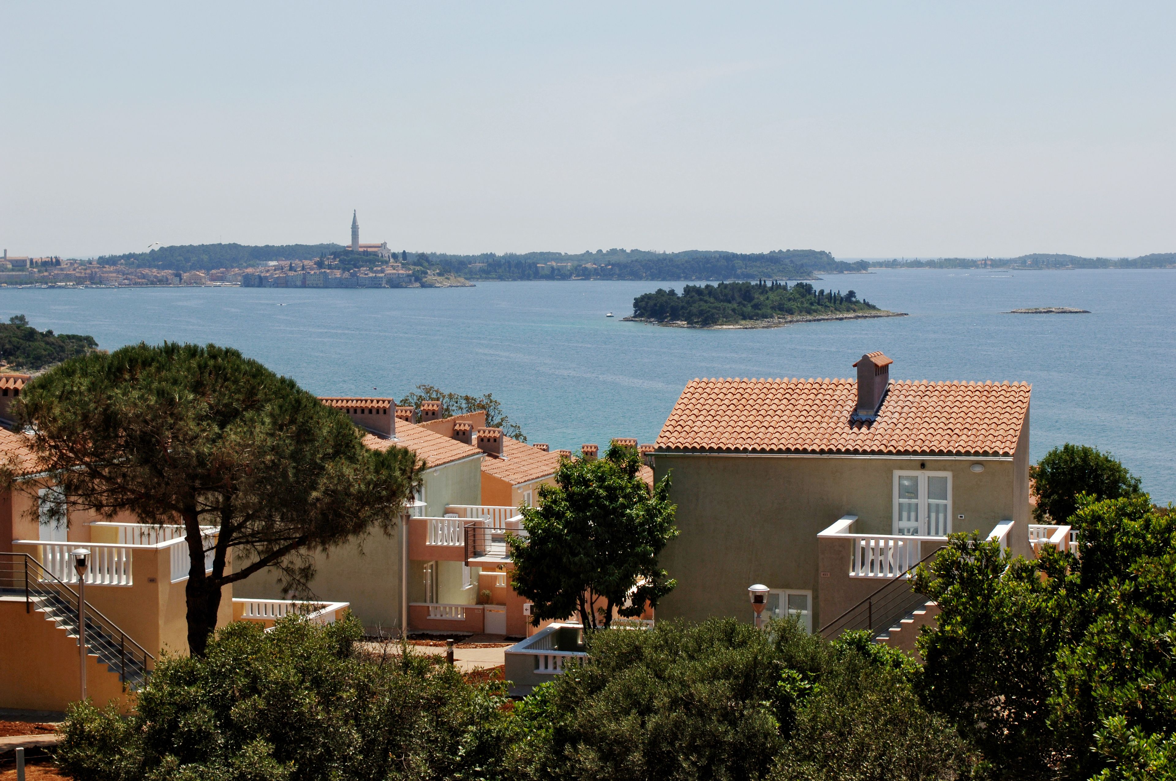 Ein Küstenwohngebiet mit terrakottafarbenen Dächern, freiem Blick auf das Meer und einer entfernten Insel.