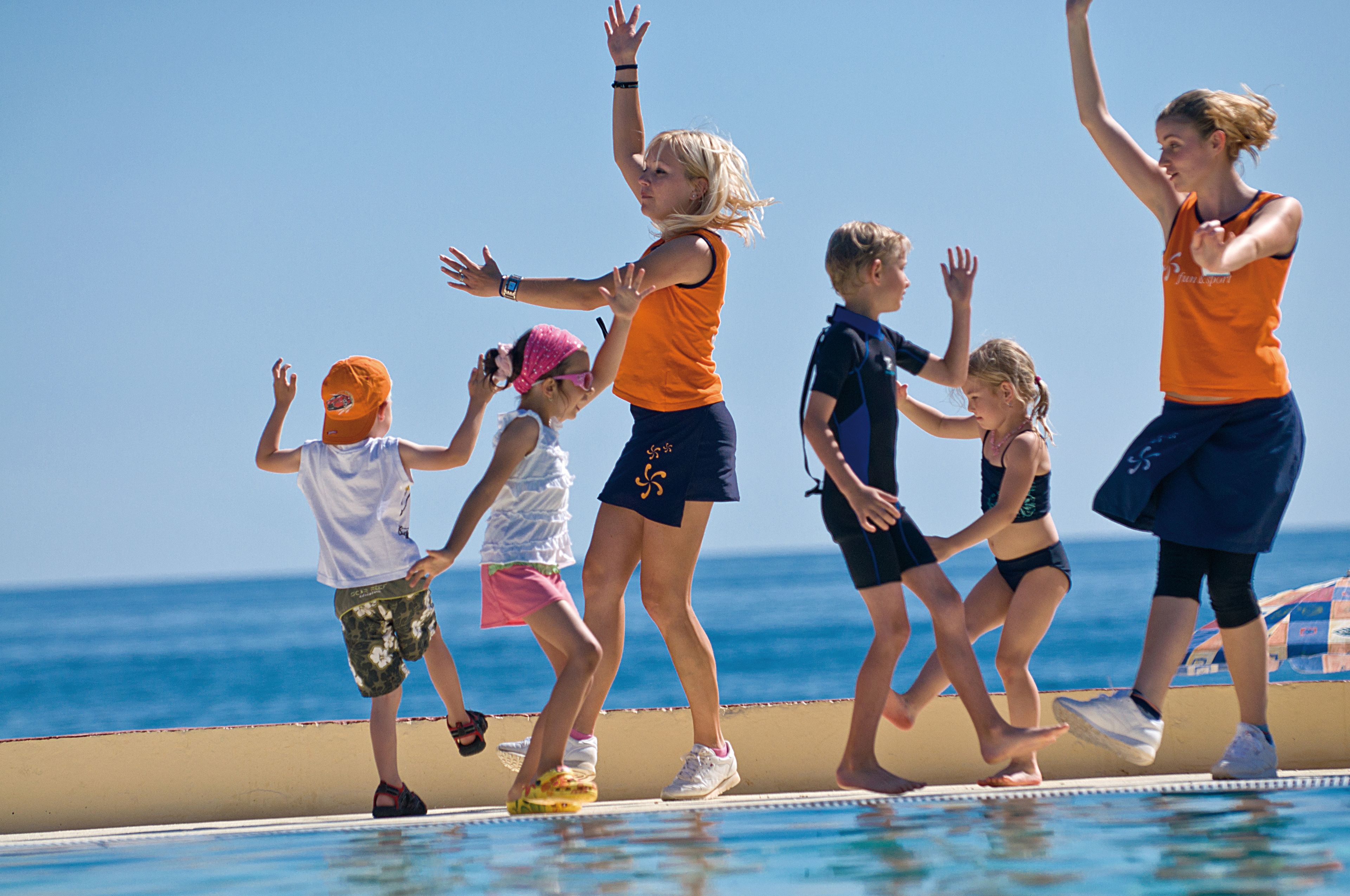Un groupe de personnes se trouve au bord d’une piscine, avec une vue dégagée sur l’océan en arrière-plan.