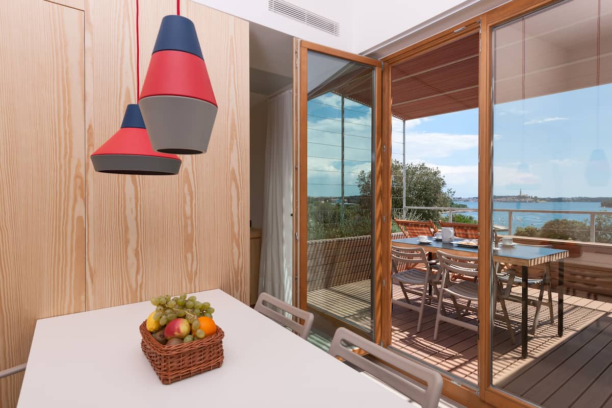 Uma área de refeições com uma mesa, cadeiras, uma cesta de frutas e vista para o exterior.