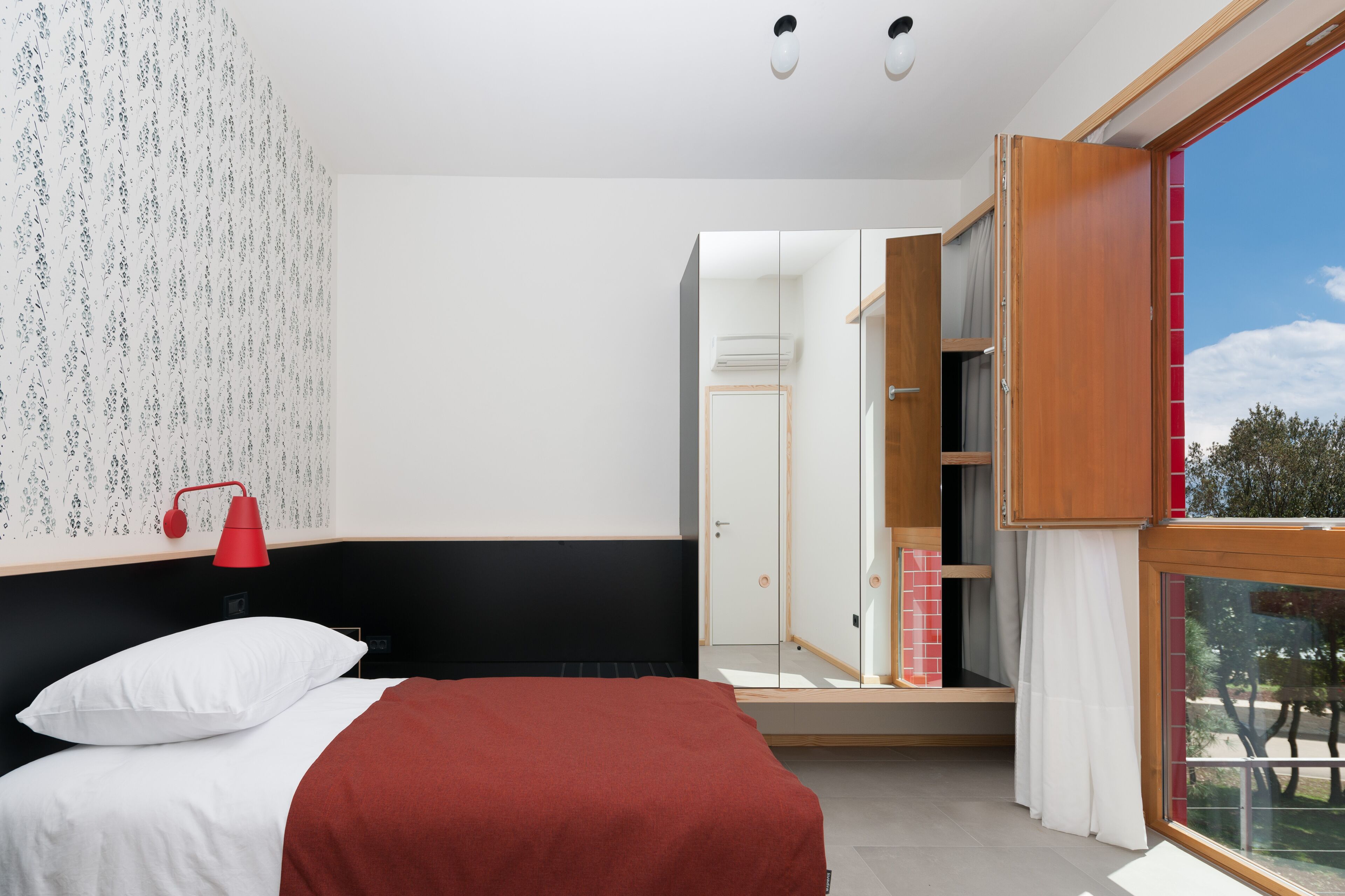 Un dormitorio con cama, lámpara roja, armario y ventana con vistas.