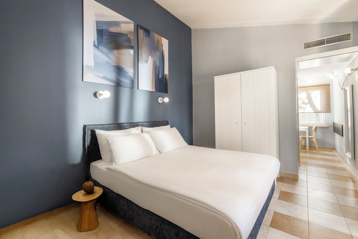Quarto moderno com uma cama grande, uma mesinha redonda e arte abstrata na parede.