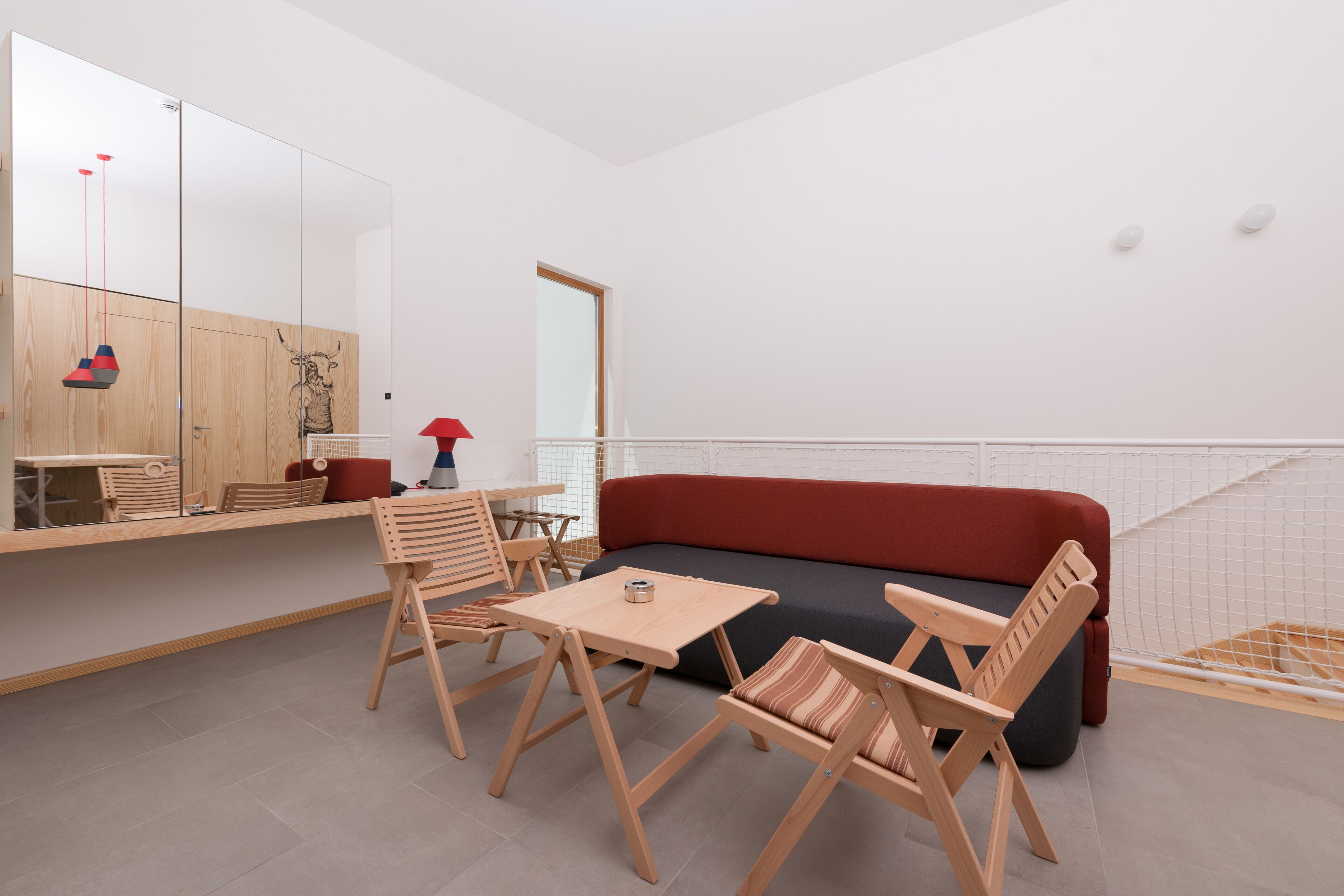 A modern room with a wooden table, two chairs, a red sofa, and a large mirror.
