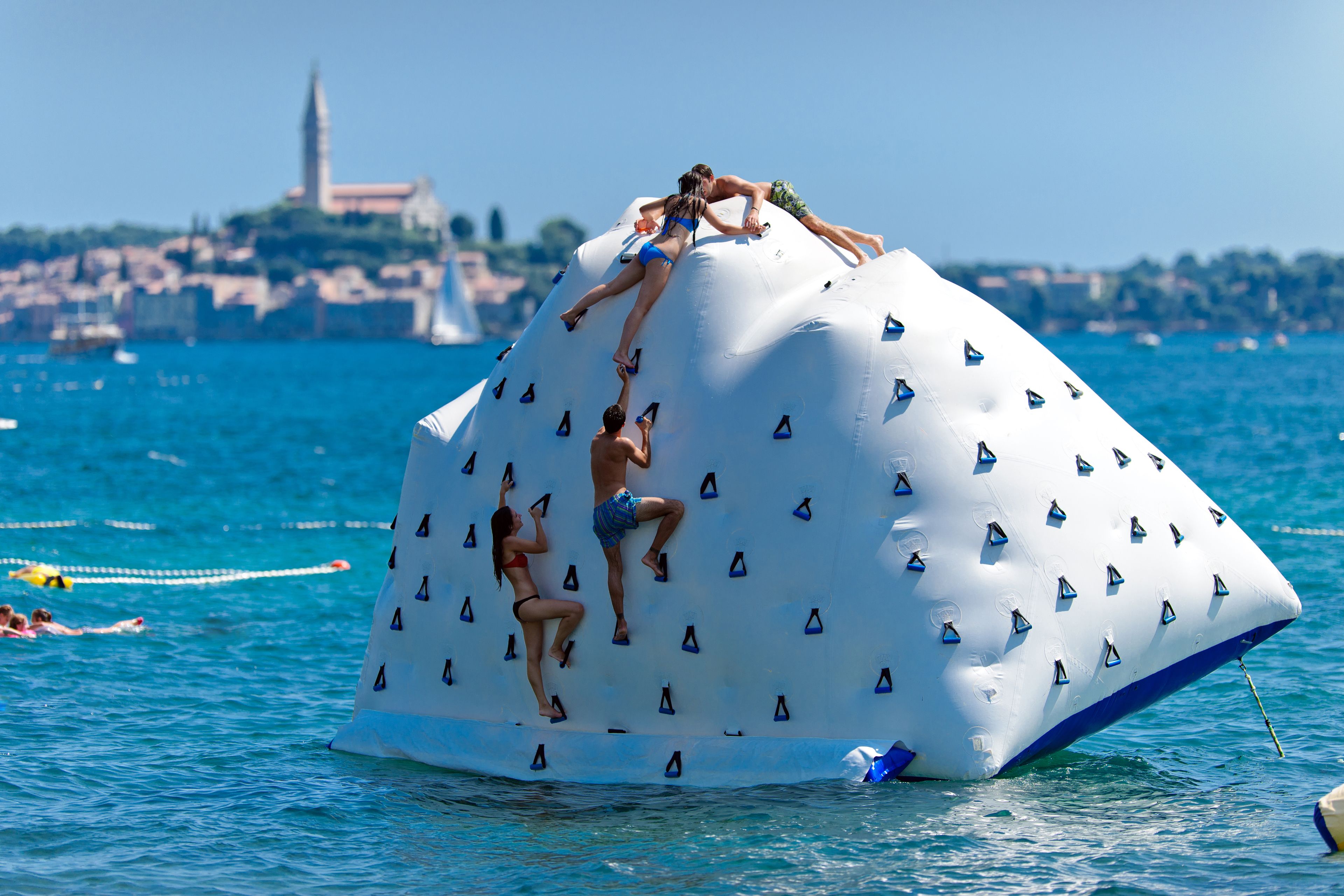 Una gran estructura inflable para escalar rocás en el agua, con gente escalando.