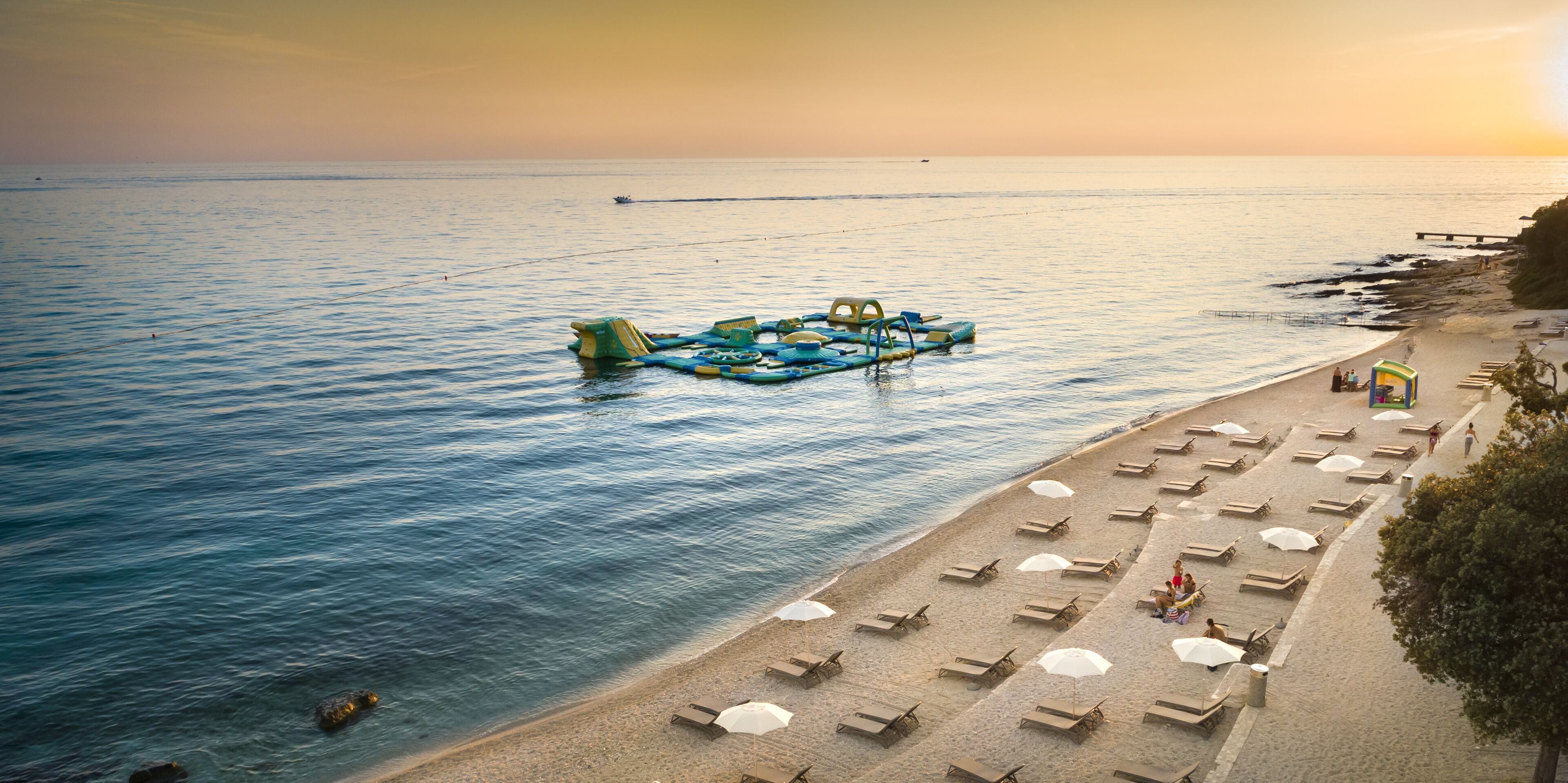 A beach with sun loungers and umbrellas, a floating structure, and a pier.