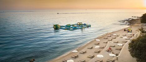 A beach with sun loungers and umbrellas, a floating structure, and a pier.