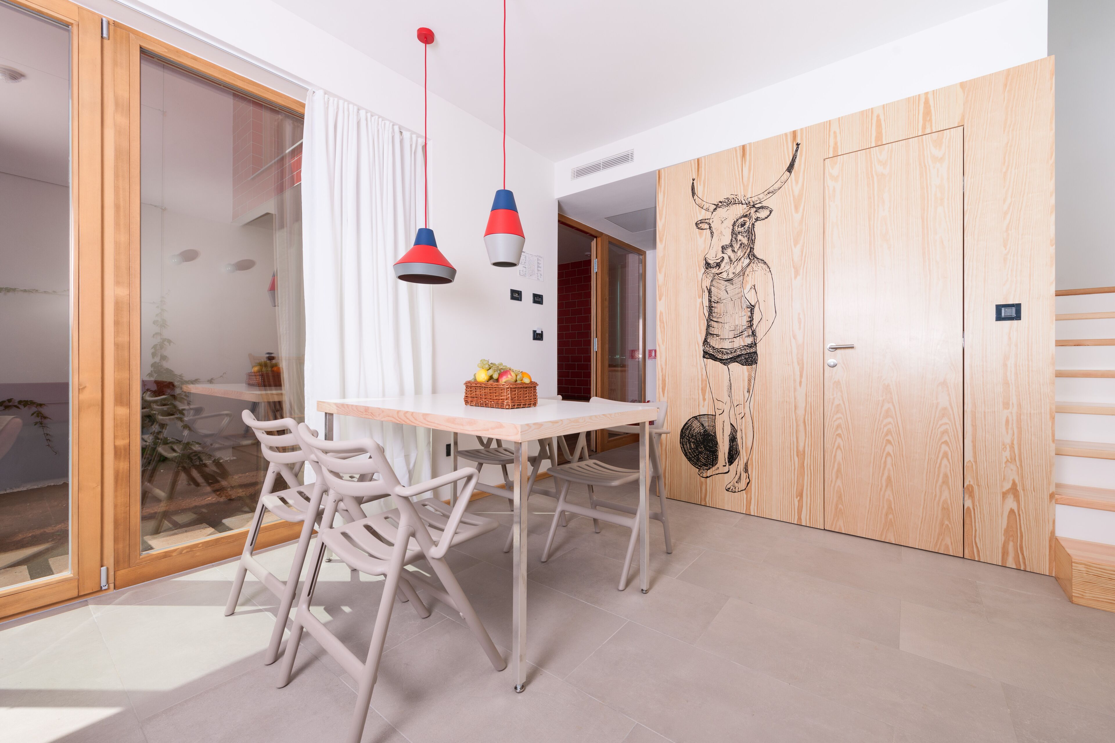 A modern dining area with a wooden table, white chairs, and a red and white pendant light.