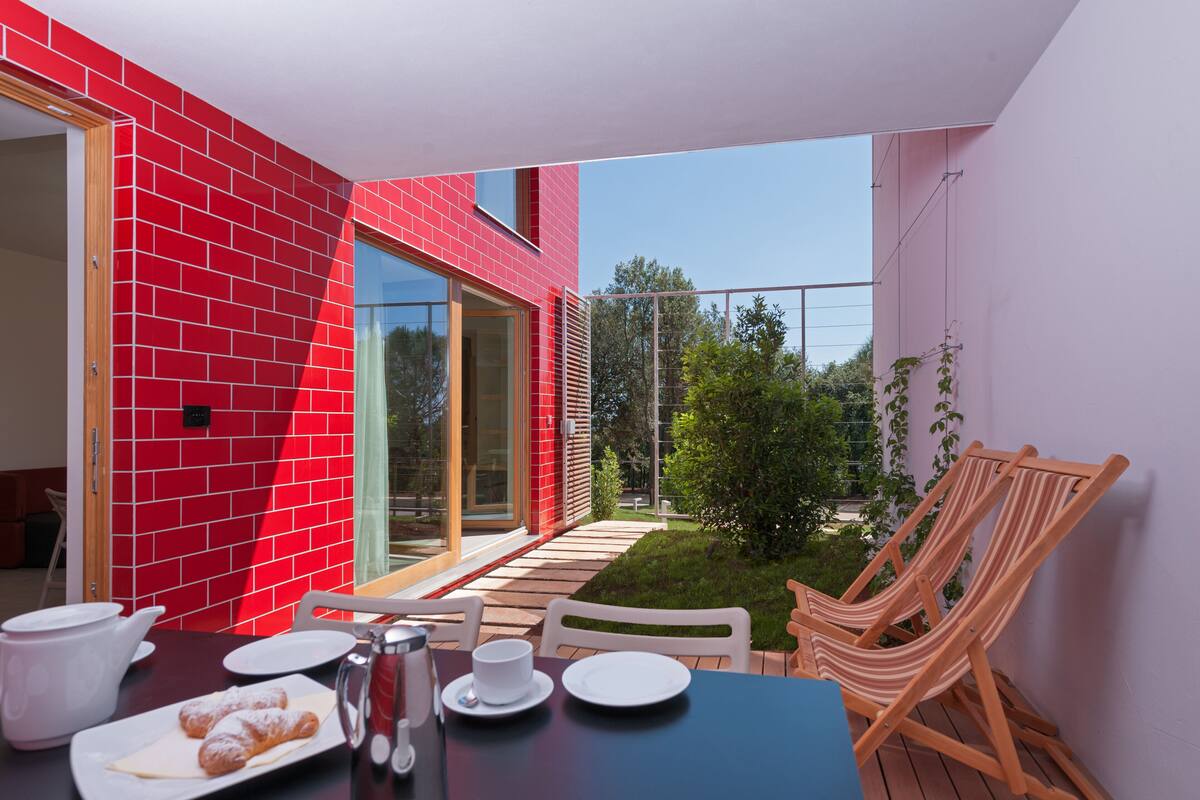 Uma sala de jantar com mesa posta para dois, parede de tijolos vermelhos e vista para o jardim.