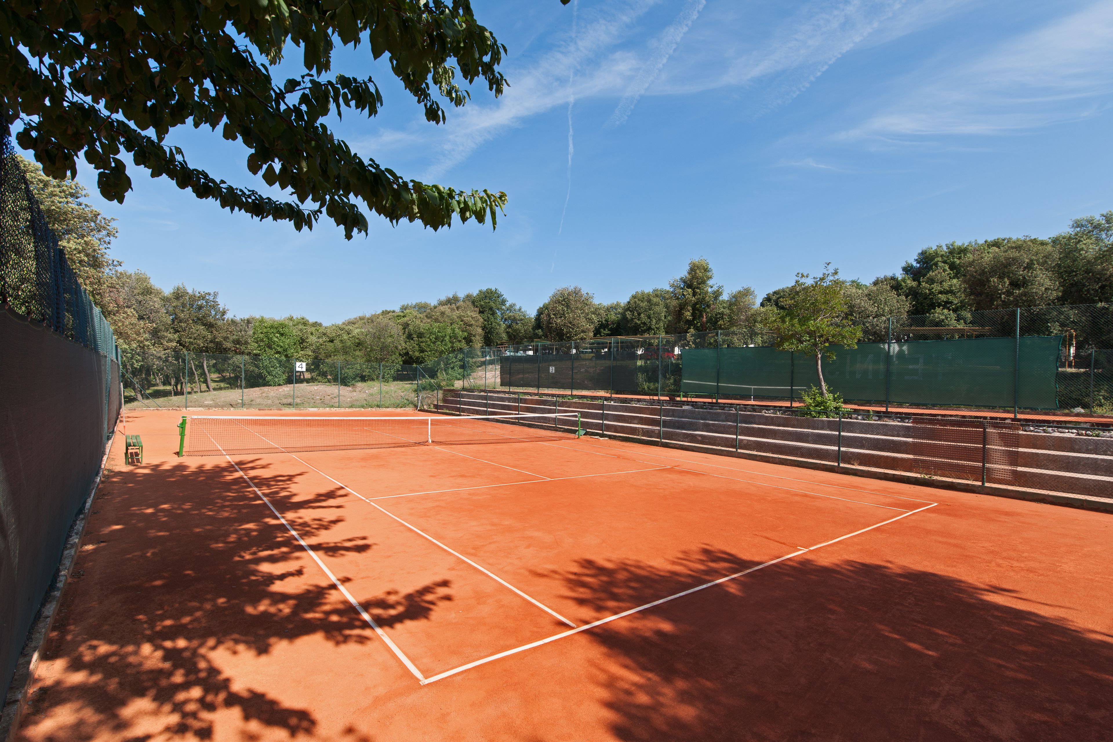 A tennis court with a net, surrounded by trees and a fence.