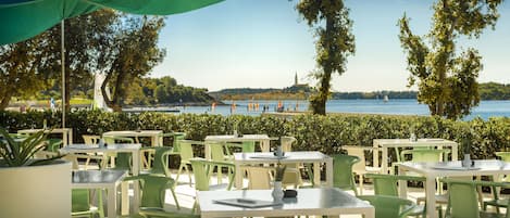 Outdoor seating with tables and chairs, a view of the water, and trees.