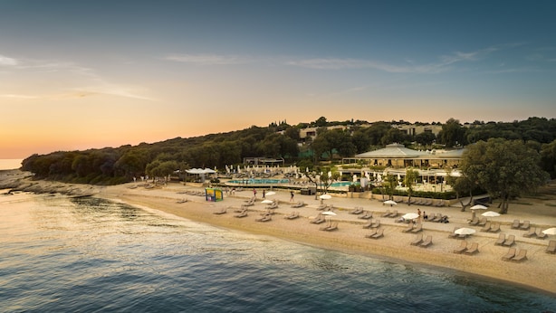 Un complexe hôtelier de bord de mer doté d’une piscine, de chaises longues et offrant une vue sur la mer au coucher du soleil.