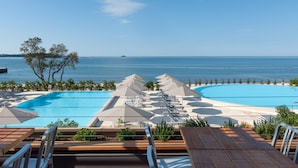 Un espace piscine avec des chaises longues et des parasols, une terrasse en bois et une vue sur la mer.