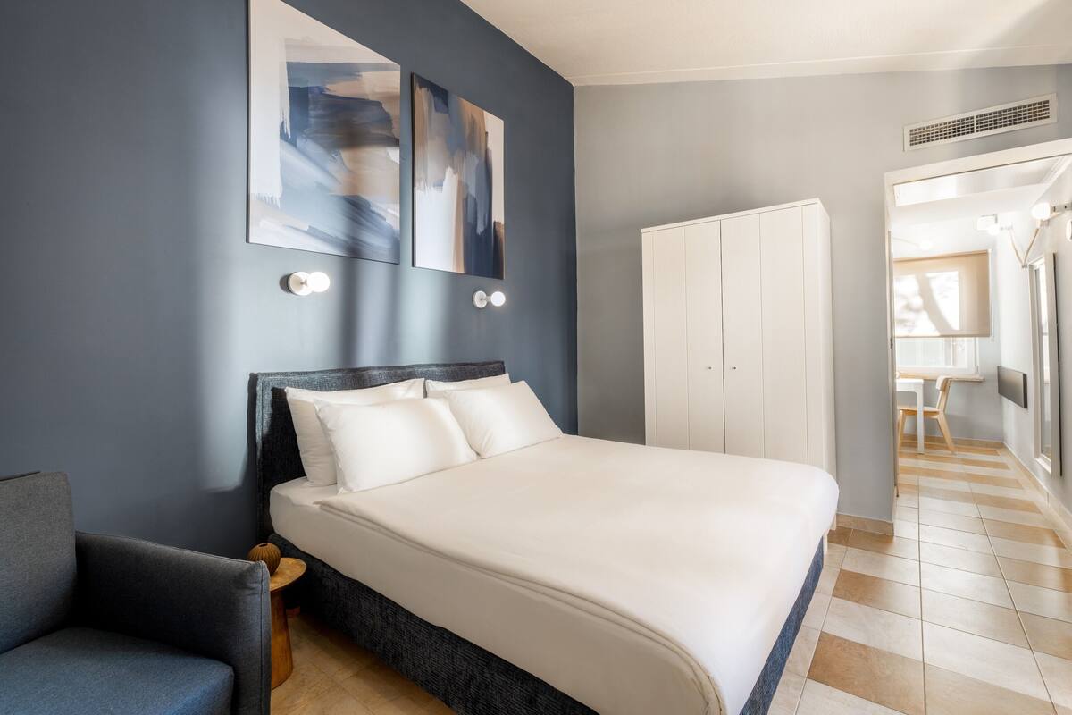 Quarto moderno com uma cama grande, uma poltrona cinza e arte abstrata nas paredes.
