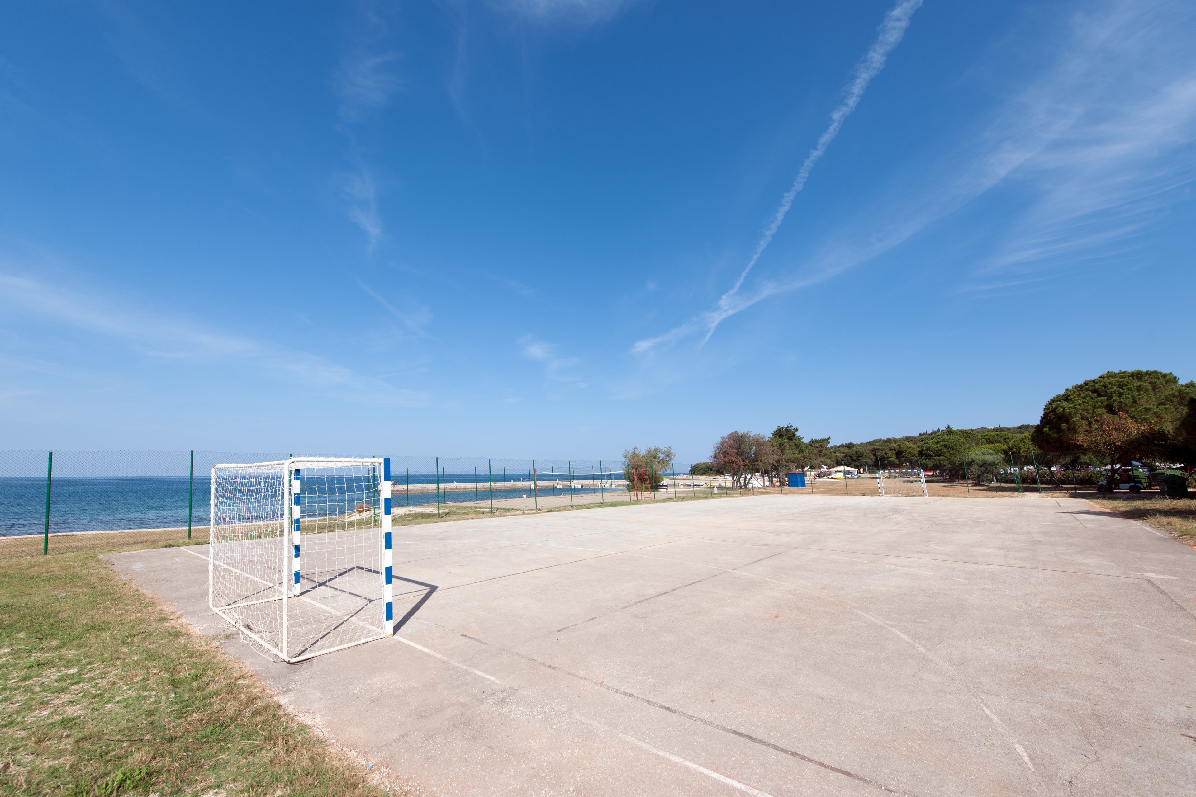 A concrete sports court with a goalpost, a clear sky, and a distant view of the sea.