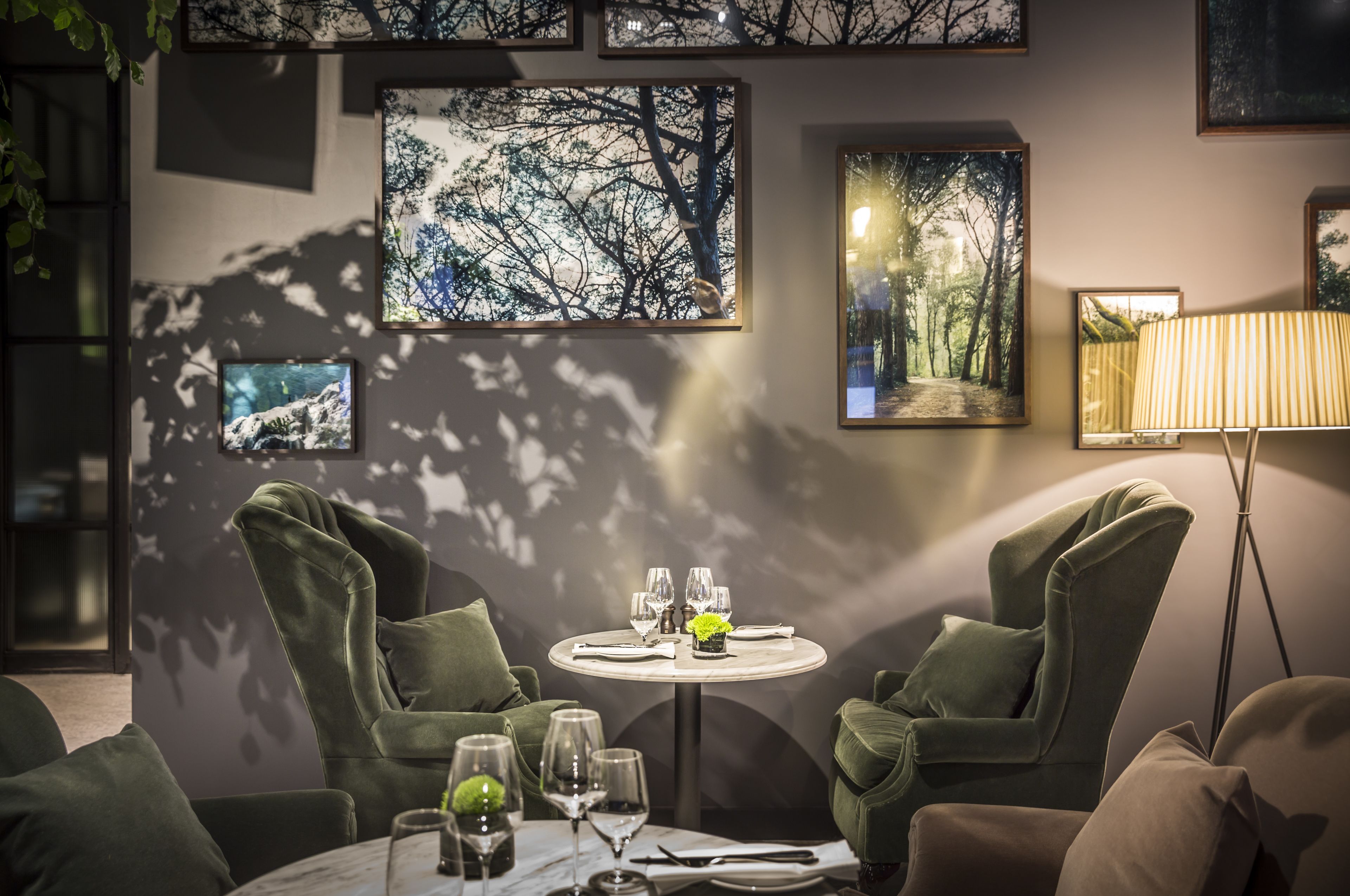 A dining area with a round table set for two, surrounded by green upholstered chairs.