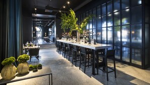 Un restaurante moderno con una barra larga, sillas negras y un amplio ventanal con vistas.