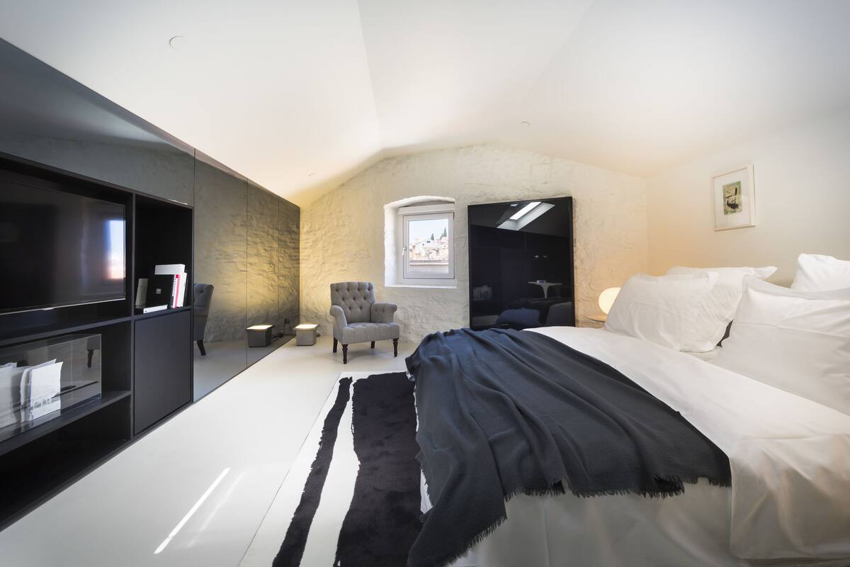 A modern bedroom with a large bed, a TV, a chair, and a small window.