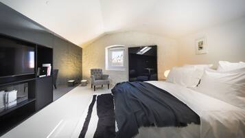 Un dormitorio moderno con una cama grande, televisión, una silla y un ventanal pequeño.