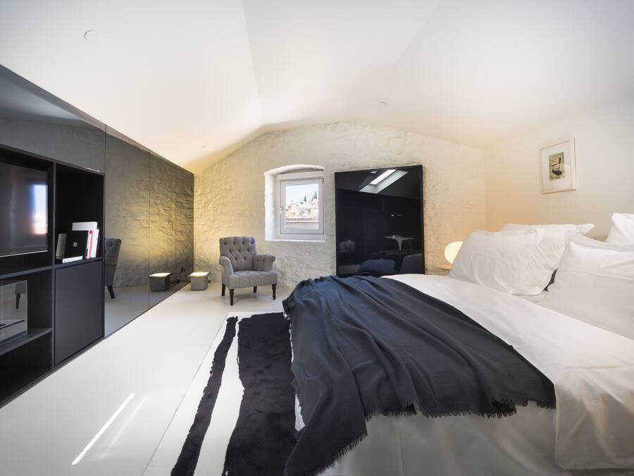 A modern bedroom with a large bed, a TV, a chair, and a small window.