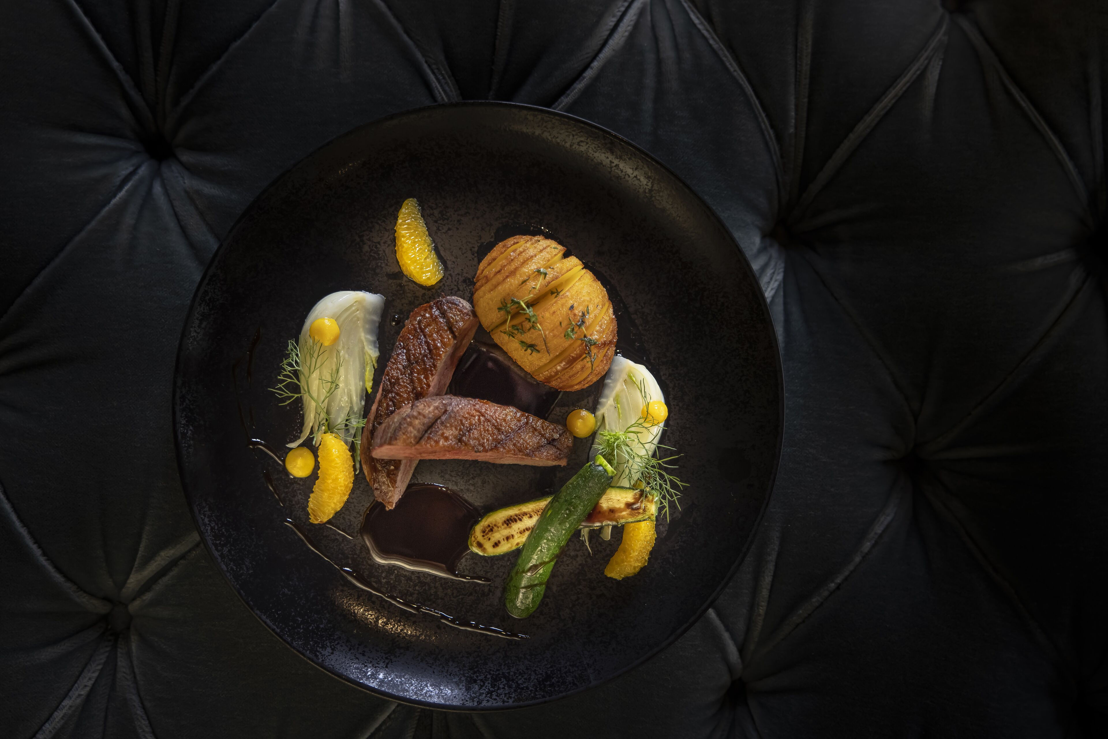 A black plate with various food items on a dark, tufted surface.