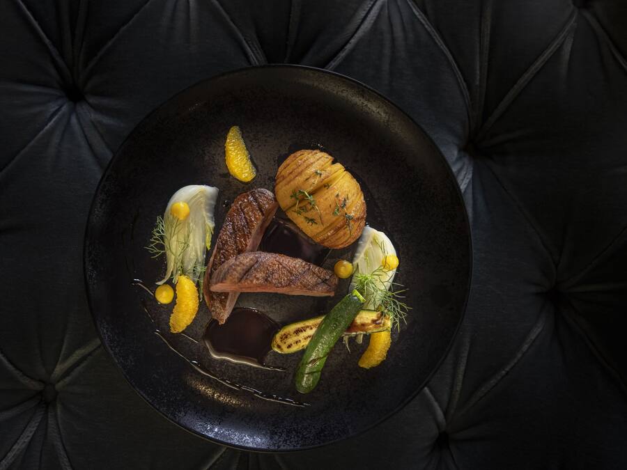 A black plate with various food items on a dark, tufted surface.
